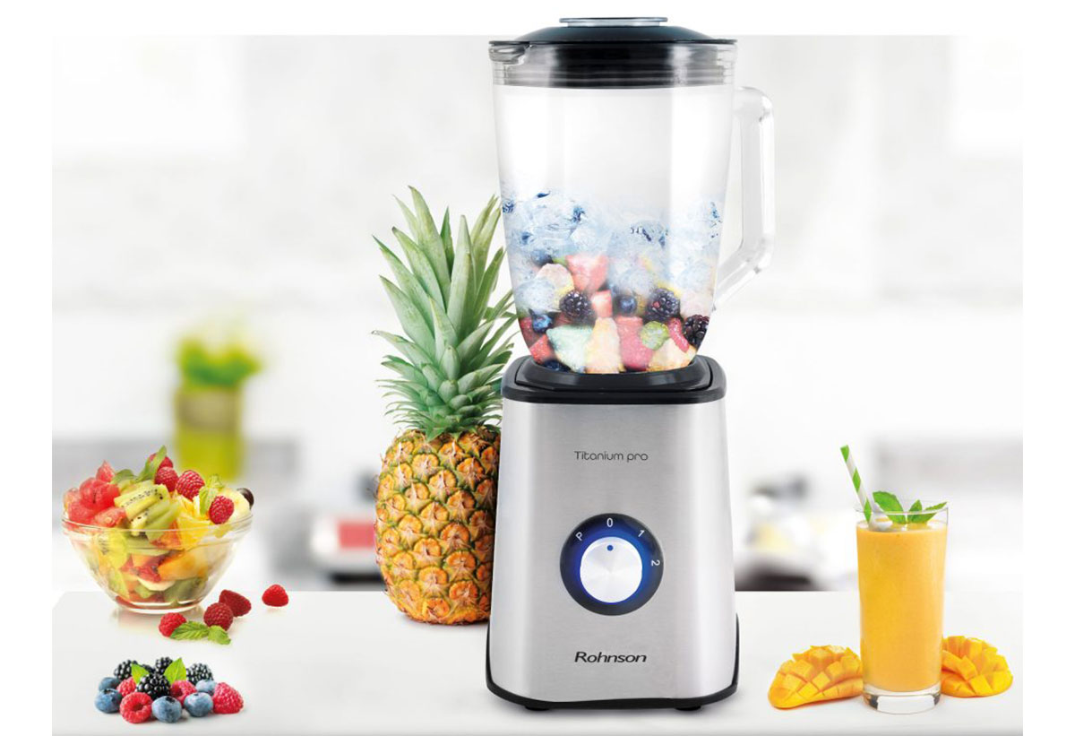 Απεικονίζει το μπλέντερ σε ένα πάγκο κουζίνας με διάφορα φρούτα εν ώρα λειτουργίας